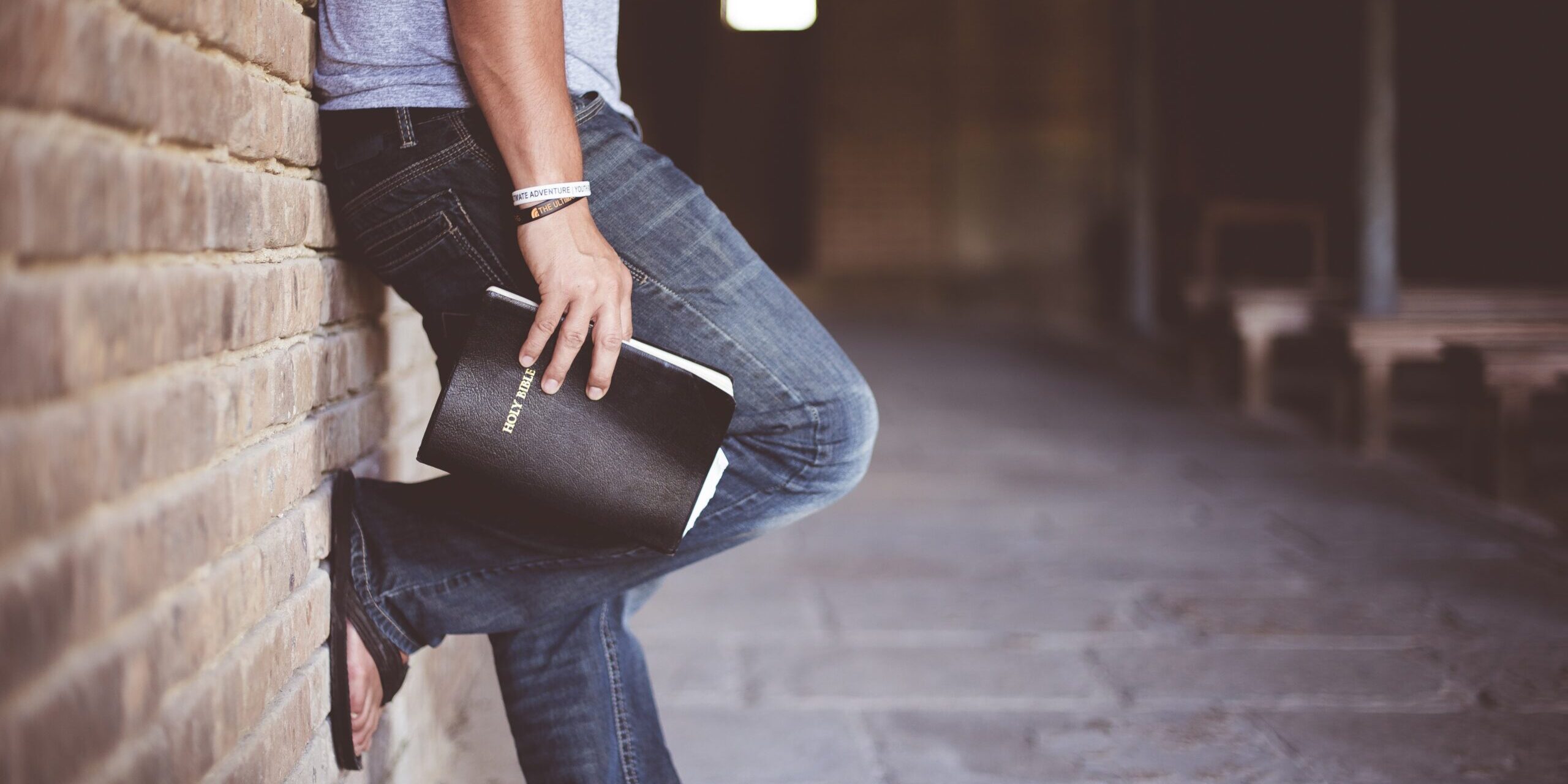 Billede af en person, lænet op af væggen i en kirkelignende bygning med en bibel i hånden